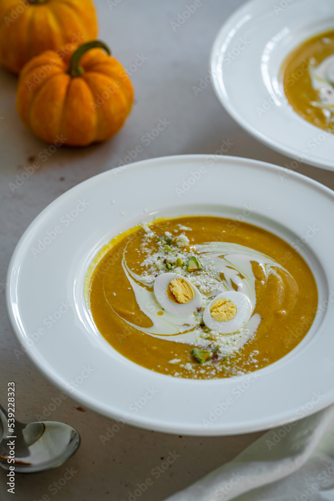 Homemade pumpkin cream soup with quail eggs, parmesan , sour cream and pistachios on white background Homemade pumpkin cream soup with quail eggs, parmesan , sour cream and pistachios on white background