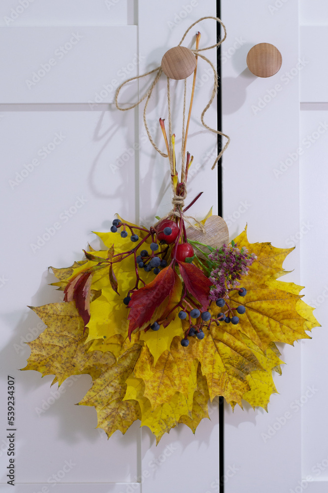 Obraz premium Autumn colorful leaves bouquet hang on white door