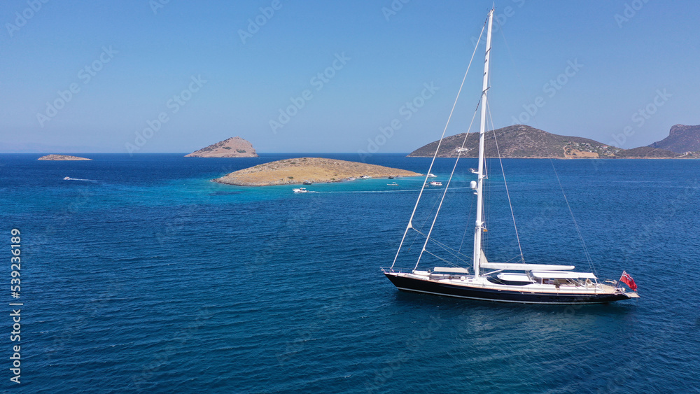 Aerial drone top down photo of beautiful sailing boat anchored in deep blue sea of Mykonos island, Cyclades, Greece Aerial drone top down photo of beautiful sailing boat anchored in deep blue sea of Mykonos island, Cyclades, Greece