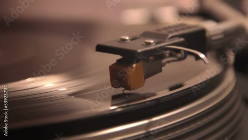 close-up of a turntable head that rides on a vintage spinning vinyl record plank. Needle playing on a lp