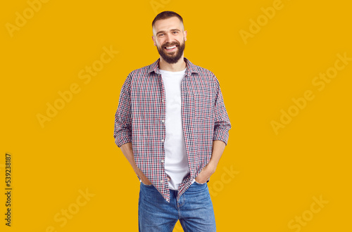 Men's casual style. Portrait of handsome smiling Caucasian young man in stylish comfortable casual clothes. Bearded man in jeans, t-shirt and shirt smiling looking at camera on orange background.