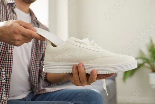 Young man puts clean orthotic insole inside his modern white comfortable orthopedic shoe that he is holding in his hand. Cropped shot. Foot arch support, pain treatment and flatfoot prevention concept photo