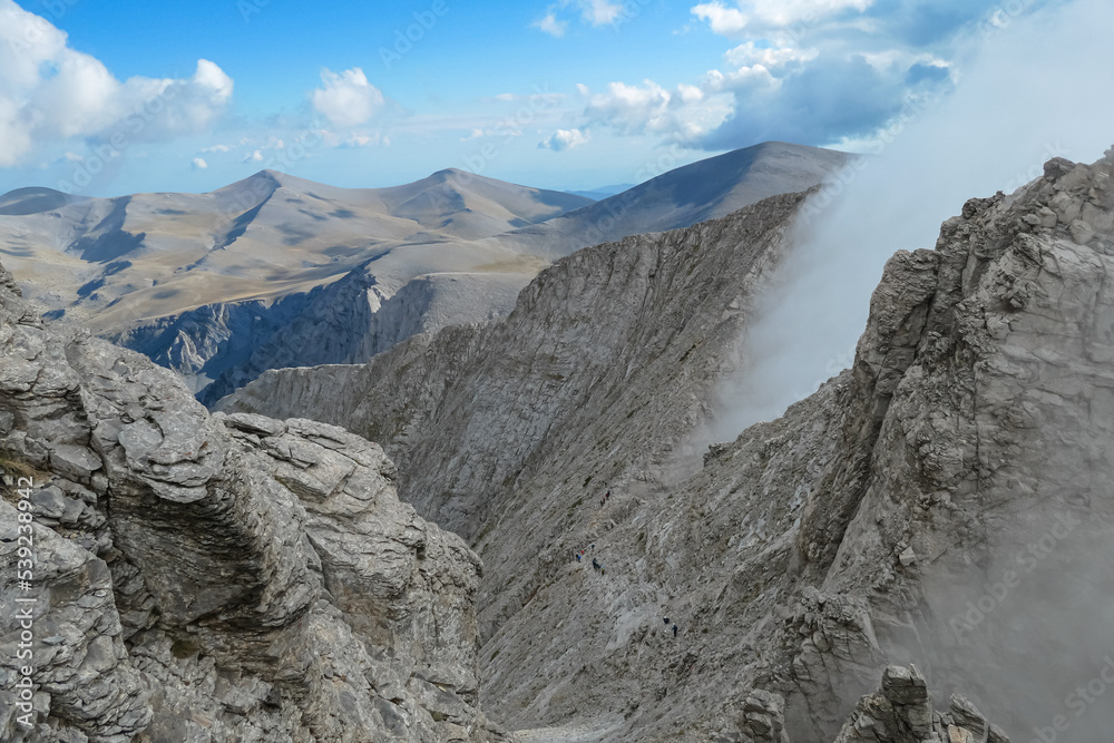 Panoramic view from cloud covered mountain summit Mytikas Mount Olympus, Mt Olympus National Park, Macedonia, Greece, Europe. Home of the Ancient Greek gods. Hiking trail from Skala, Skolio, Stefani