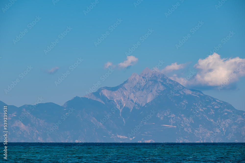 Panoramic early morning view of cloud covered holy Mount Athos from Fava sand beach, Vourvourou, peninsula Sithonia, Chalkidiki (Halkidiki), Greece, Europe. Summer vacation at Aegean Mediterranean Sea