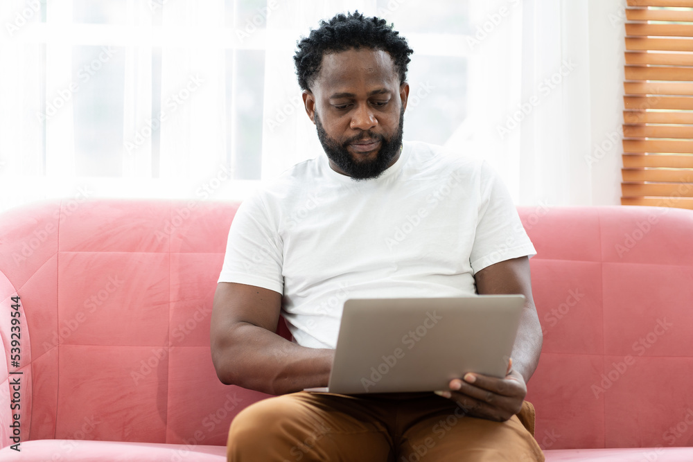 African American male working with laptop computer on sofa at home African American male working with laptop computer on sofa at home