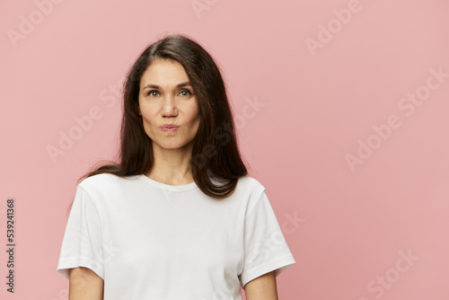 portrait of a cute, attractive brunette in a white tank top on a pink background, with an emotional face showing a grimace
