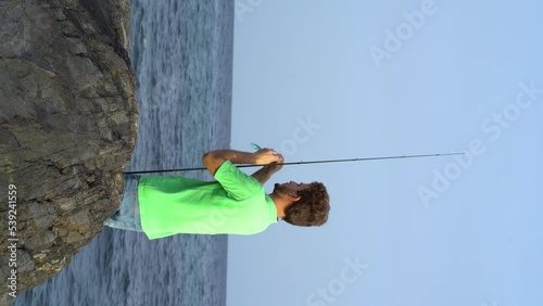 fisherman preparing the line for fishing, vertical video, fisherman with his back on some rocks, the sea in the background