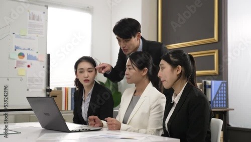 asian four businesspeople having group discussion about new startup plan in creative office. male partner pointing out an issue on the computer