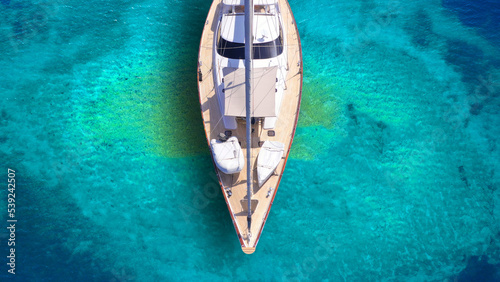 Aerial drone top down photo of beautiful luxury sail boat with wooden deck anchored in turquoise paradise island beach forming a blue lagoon © aerial-drone