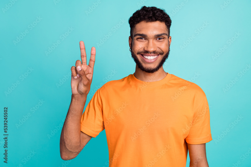 Photo of attractive positive man toothy smile wear orange clothes arm demonstrate hi v-sign empty space isolated on cyan color background Photo of attractive positive man toothy smile wear orange clothes arm demonstrate hi v-sign empty space isolated on cyan color background