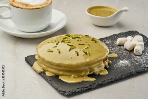 Closeup of pancakes covered with pistachio paste and sprinkles served with coffee