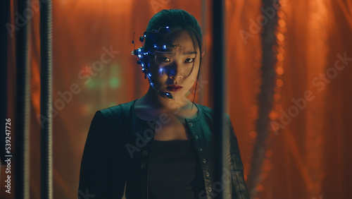 Cyberpunk girl in a black leather jacket trapped behind black hanging rods. Intense facial expressions. Asian girl with futuristic glasses and headset. Cyborg, sci-fi, Neon lights.