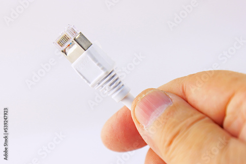 The hand holds a color-coded Ethernet wire with an RJ45 connector on a white background.Soft focus.