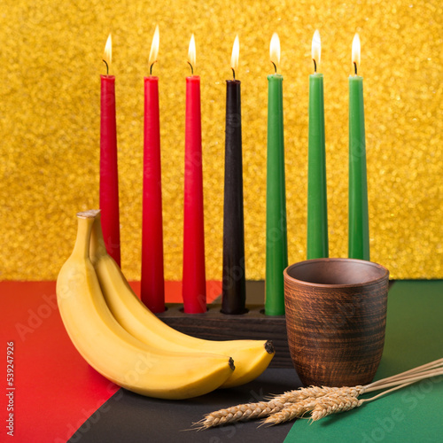 African Kwanzaa holiday concept with traditional lit candles, banana, bowl and ears of wheat photo