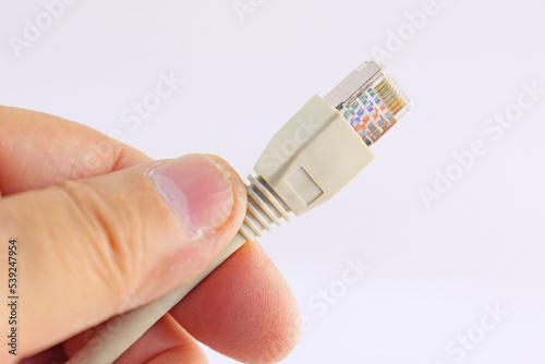 The hand holds a color-coded Ethernet wire with an RJ45 connector on a white background.Soft focus.
