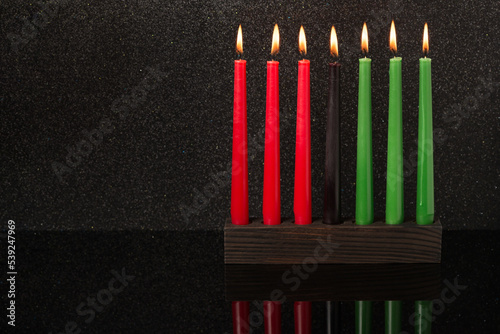 Kwanzaa festival concept with seven candles red, black and green in candlestick with reflection on black background, copy space