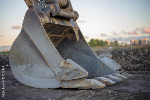 The metal bucket of a parked excavator lies on the ground soiled after work. Excavator bucket with large teeth close-up side view. Heavy construction equipment.
