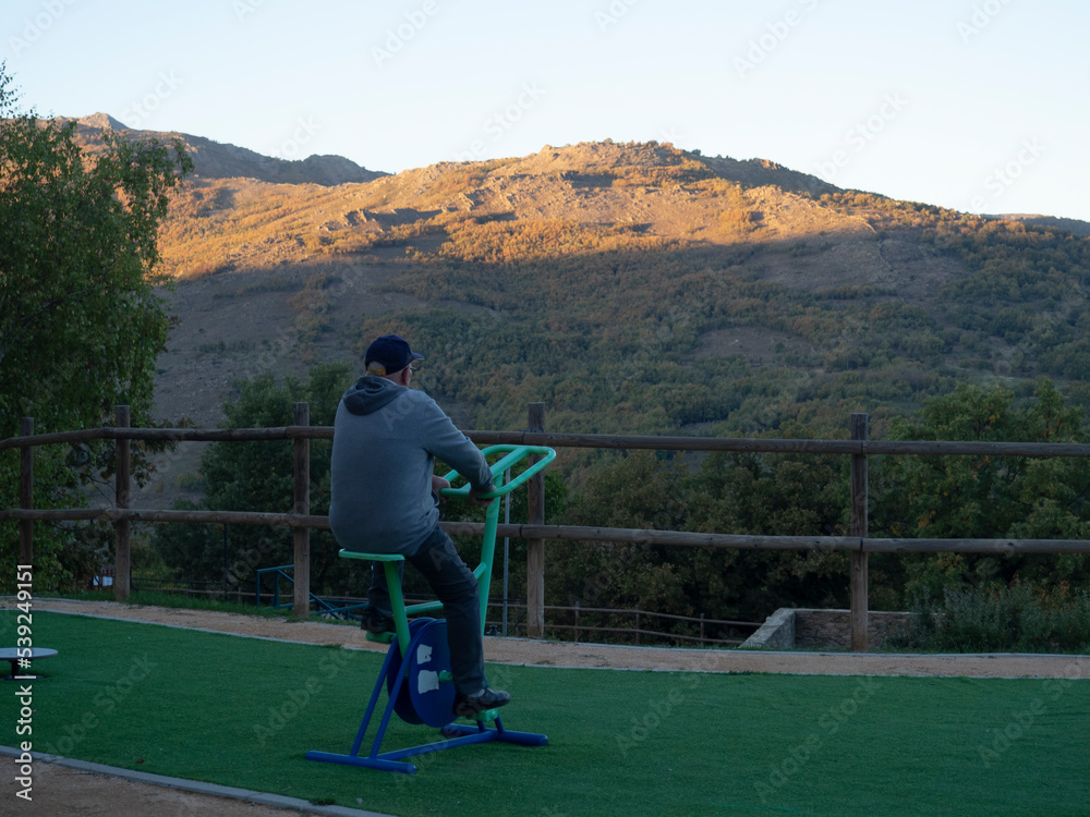 Obraz premium Anciano haciendo ejercicio como propósito de año nuevo, en un parque, al aire libre rodeado de montañas, en un espacio adaptado para la gente mayor, otoño de 2022 Madrid.