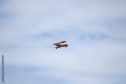 Fototapeta Naklejka Na Ścianę i Meble -  Little red biplane flying across semi cloudy sky. This plane almost reminded me of the red baron. It has such an old look to it. I took this picture while standing on the beach in Cape May New Jersey.
