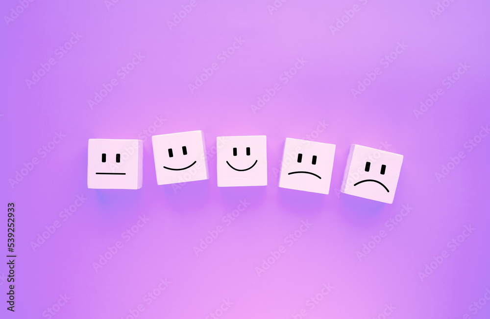 The face satisfaction survey concept shows the emotional level of satisfaction. Emoticon face on white wooden blocks blue background The face shows the emotional level of satisfaction. The face satisfaction survey concept shows the emotional level of satisfaction. Emoticon face on white wooden blocks blue background The face shows the emotional level of satisfaction.
