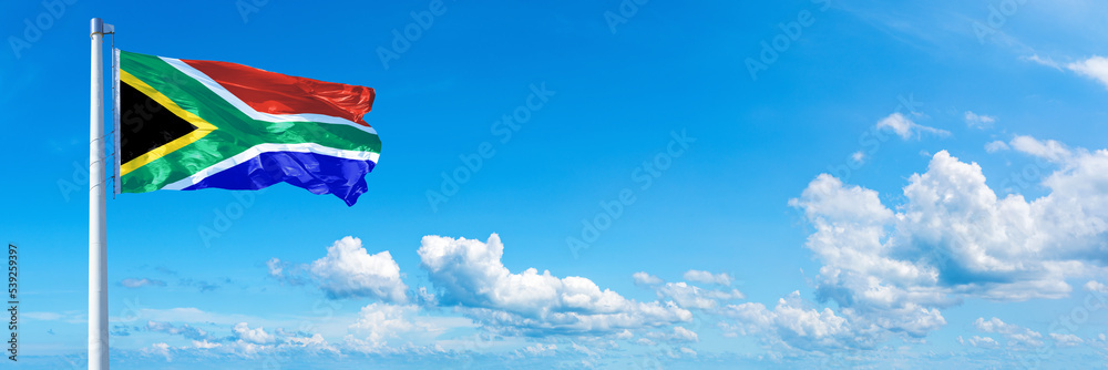 Obraz premium South Africa flag waving on a blue sky in beautiful clouds - Horizontal banner