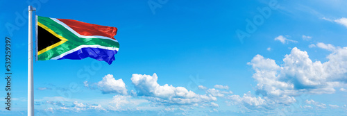 South Africa flag waving on a blue sky in beautiful clouds - Horizontal banner