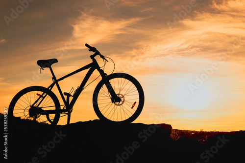 silhouette of a bicycle on a hill, wheels in the grass and sunlight