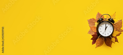 Autumn composition sale banner with dried leaves and black alarm clock on pastel yellow background. Autumn, fall Flat lay, top view, copy space photo