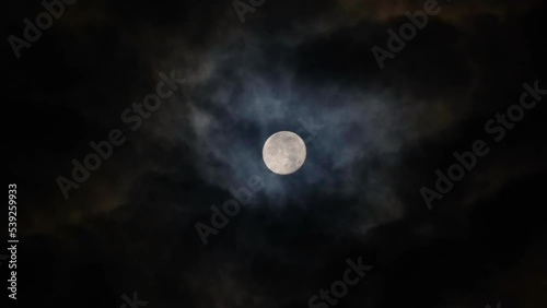 Full Moon on a black cloudy night. Colored clouds passing by the Moon in spooky feeling like thriller and horror films. Dark night sky. Real video recording