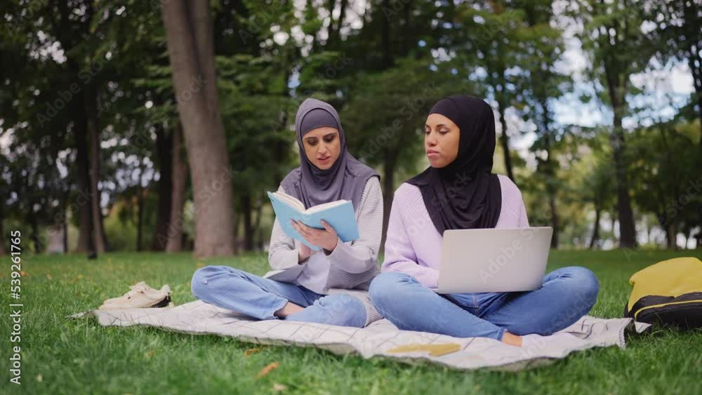 Two Arab women in hijabs studying in park, friends hanging out outdoors Two Arab women in hijabs studying in park, friends hanging out outdoors