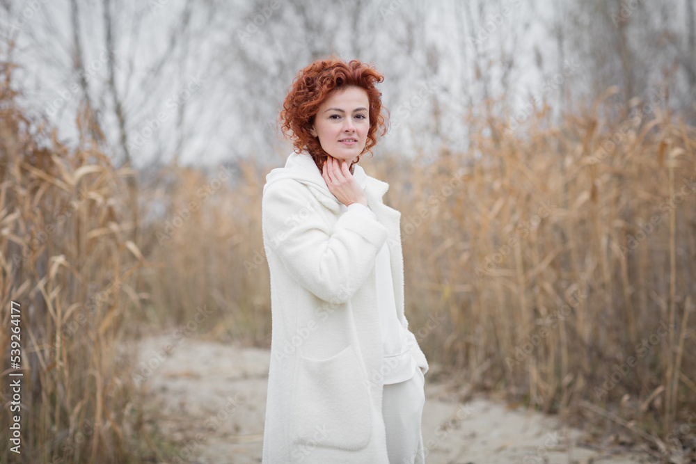 Autumn portrait. Happy redhair woman in white clothes is looking at camera and smiling while walking in the park Autumn portrait. Happy redhair woman in white clothes is looking at camera and smiling while walking in the park