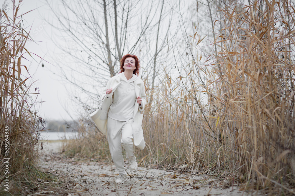 Pretty young woman in trendy white clothes poses in motion against the backdrop of an autumn landscape with dry reeds Pretty young woman in trendy white clothes poses in motion against the backdrop of an autumn landscape with dry reeds