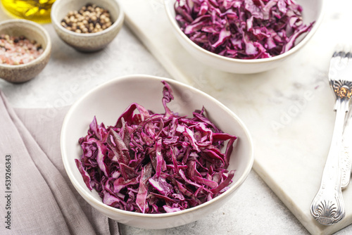 Two salad bowls with german red cabbage chopped in fine stripes on marble board on grey background