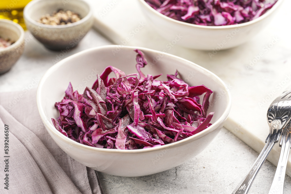 Two salad bowls with german red cabbage chopped in fine stripes on marble board on grey background Two salad bowls with german red cabbage chopped in fine stripes on marble board on grey background