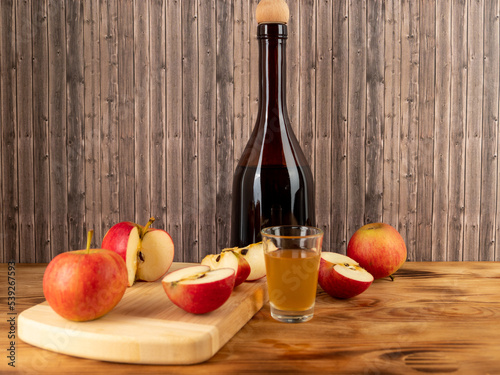 Apple cider vinegar in a bottle with apples on a wooden background.