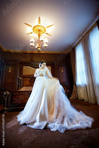 Beautiful young girl bride in a white wedding dress standing against the wall.