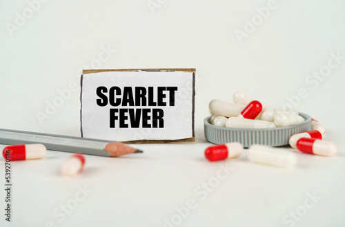 On a white background, medical capsules, a pencil and a cardboard plate with the inscription - Scarlet fever photo