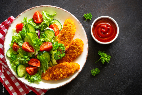 Chicken nuggets with fresh salad at black background. Top view image with copy space.