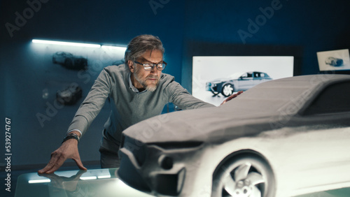 Fotografia Automotive engineer touches the model of the prototype car made of clay to make final changes in the design