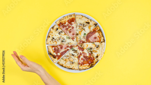 Tablou pe pânză Woman's hand near pizza on white plate. Yellow background.
