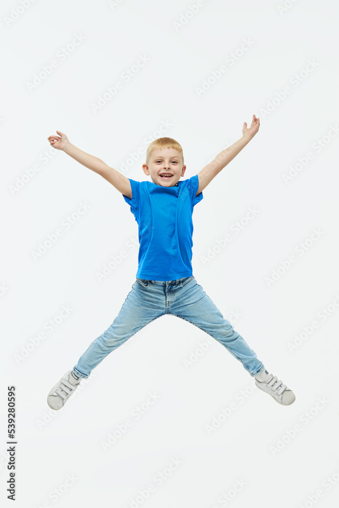 Stylish child boy model in a blue casual t-shirt joyfully jumping high on a white isolated background