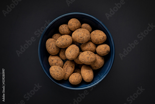 Almonds in chocolate coated in cocoa in bowl on dark table. Top view.