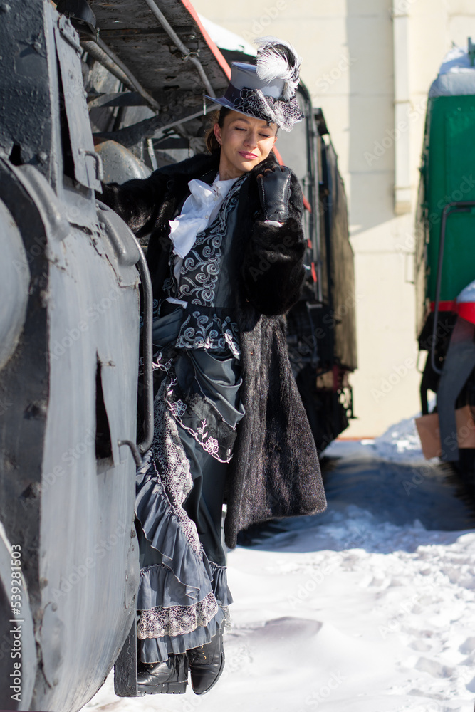 girl dressed as a noblewoman of the 19th century near a steam locomotive. Russian winter