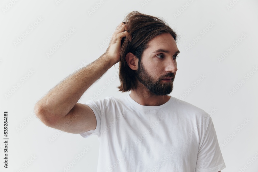 Portrait of a man with a black thick beard and long hair in a white T-shirt on a white isolated background emotion of sadness and longing
