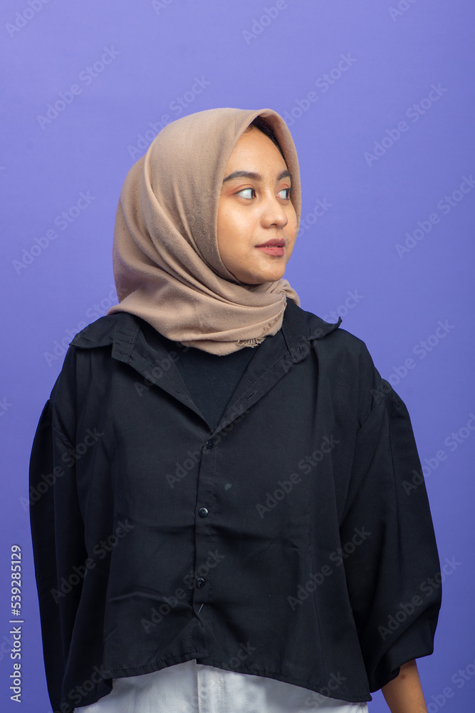 Asian Muslim Woman with Attractive Gesture Looking to Right on Purple Background Asian Muslim Woman with Attractive Gesture Looking to Right on Purple Background