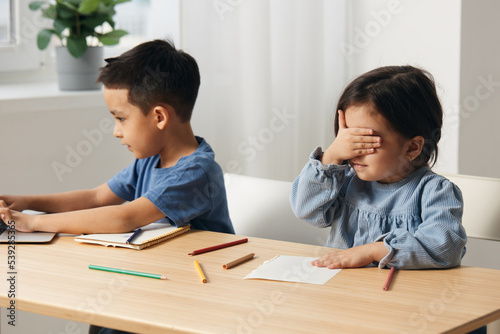 children sit at the table during class and the girl closes her eyes