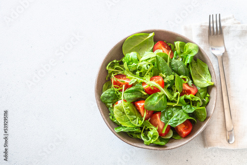 Green salad with fresh leaves and tomatoes on white kitchen table. Top view, copy space.