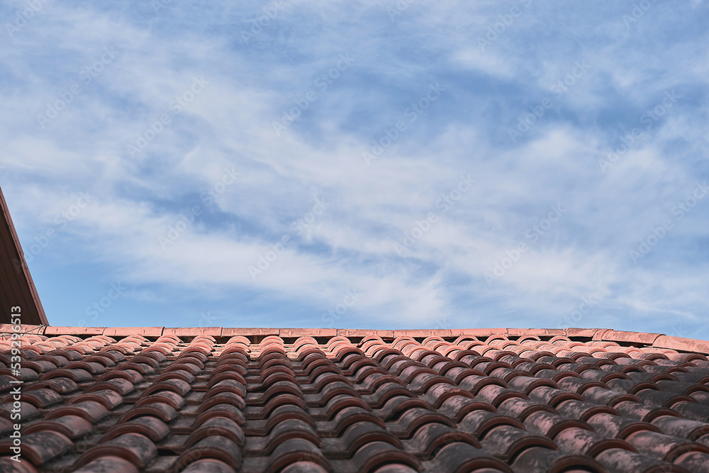 Tiled roof against a blue sky with clouds, an idea for a background with space for text. Eco-friendly traditional roofs for the home Tiled roof against a blue sky with clouds, an idea for a background with space for text. Eco-friendly traditional roofs for the home