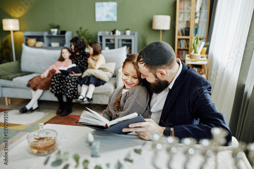 Obraz na plátně Portrait of smiling jewish father reading book to daughter while enjoying family