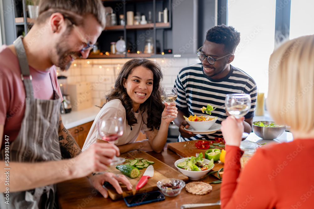 Young diverse people having a holiday party at home, preparing food, drinking, talking, and enjoying Young diverse people having a holiday party at home, preparing food, drinking, talking, and enjoying